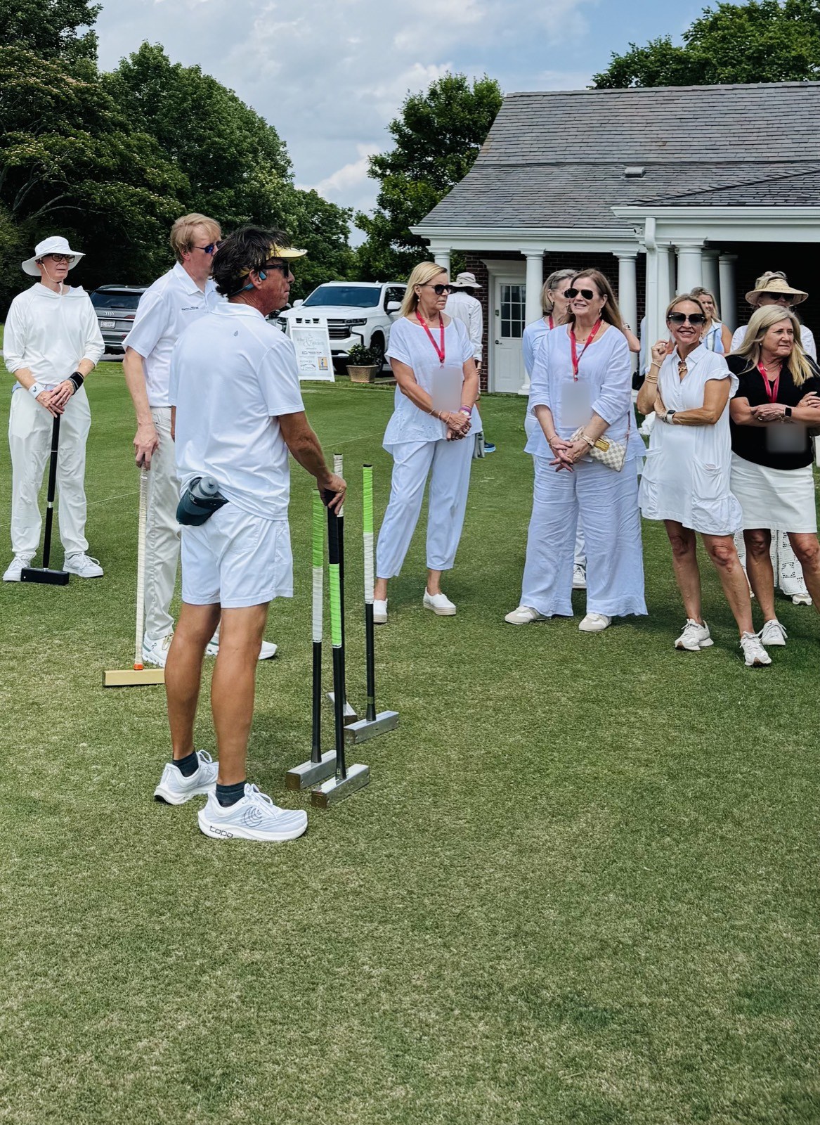 A club member standing by a row of mallets talks with guests dressed in white at the Shook Hill charity croquet afternoon.