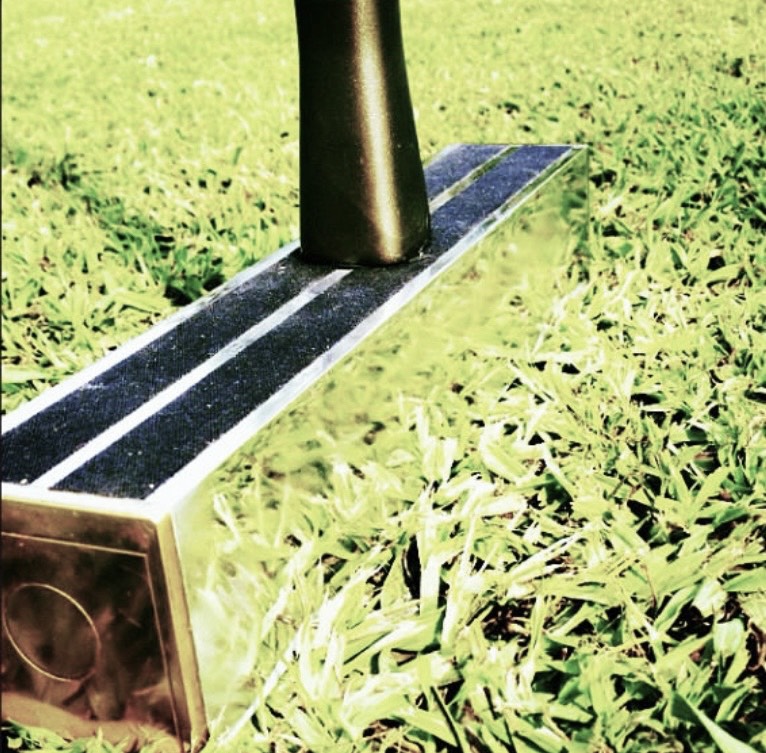Close-up of a polished metal mallet head with black grip strips along the top, resting on green grass.